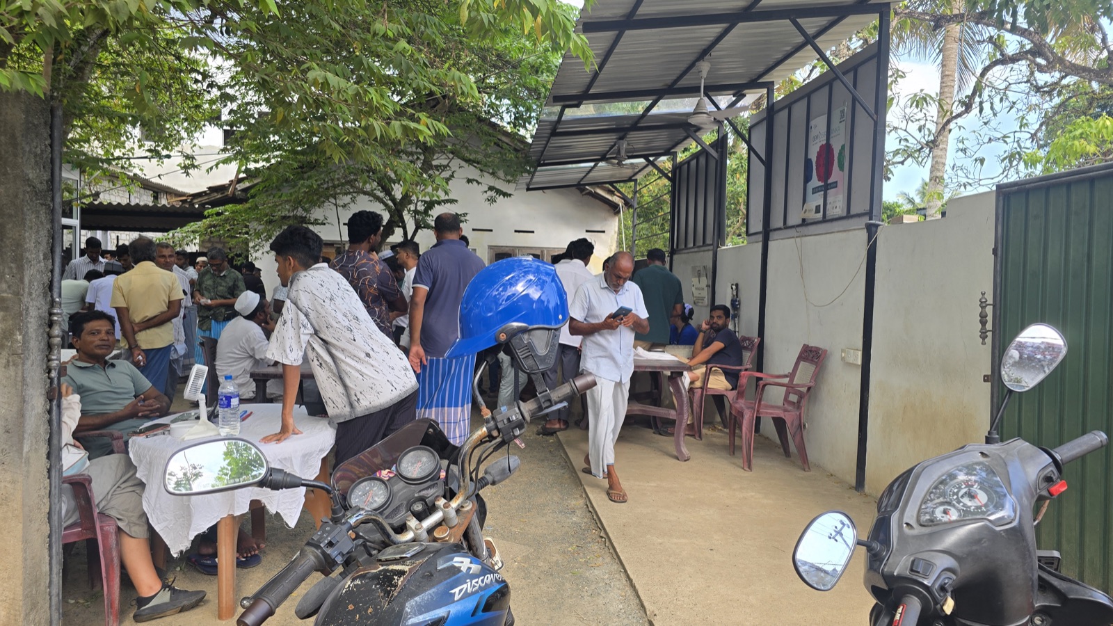 Marchands de pierres attablés sous un préau au marché aux gemmes du Sri Lanka, motos garées à l'arrière-plan
