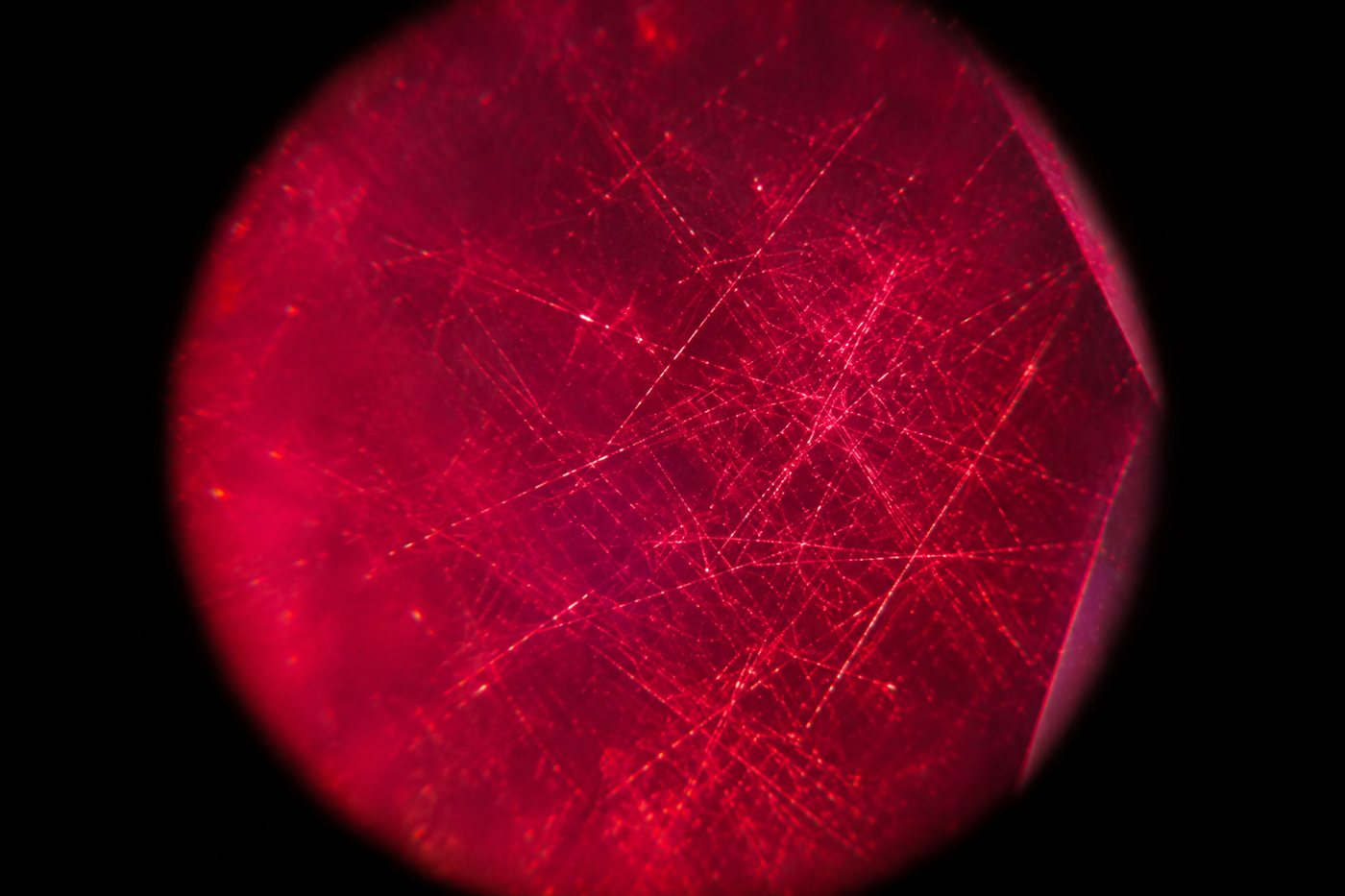 Illustration de fines aiguilles de soie qui se croisent à l’intérieur d’un rubis rouge, vues au microscope sur fond noir
